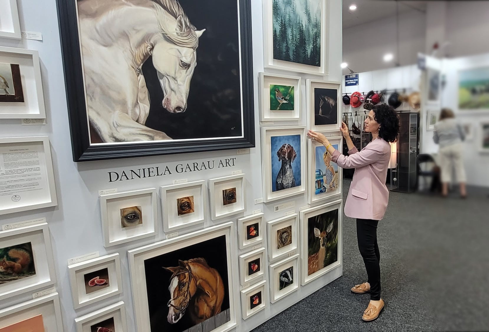 Daniela Garau adjusting her framed artworks on the wall of teh Dublin Horse Show Exhibition at RDS, Dublin
