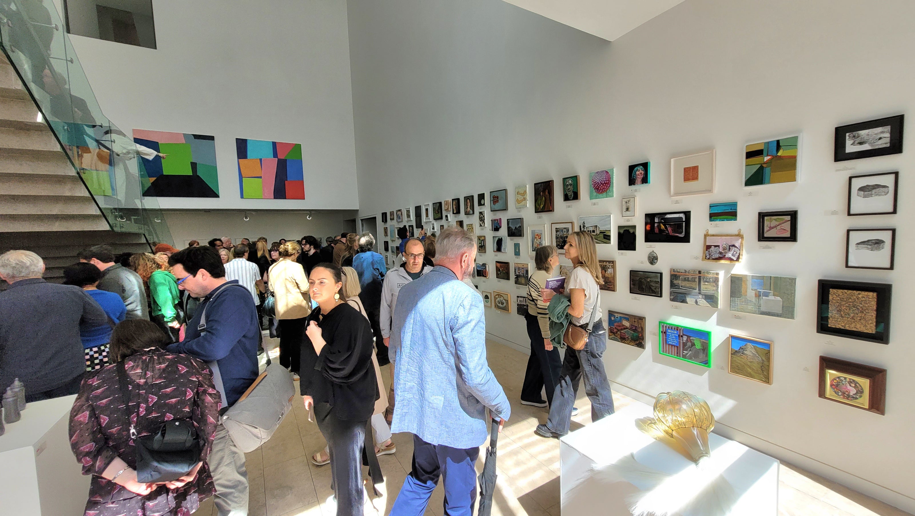 People visiting the RHA exhibition in Dublin with various paintings on the walls.